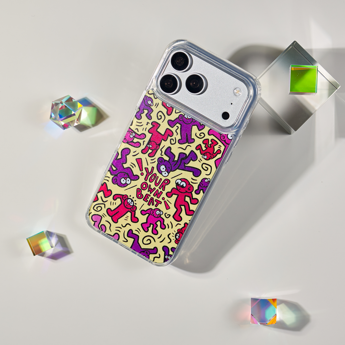 Freehand Case in Doodle Dance for iPhone 18 Pro Max, yellow design with red and purple dancing characters, shown at an angle with crystal props.