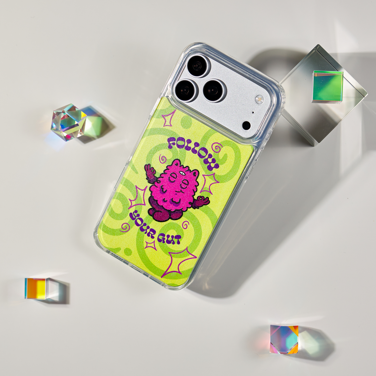 Freehand Case in Gut Feeling for iPhone 18 Pro Max, lime design with a pink illustrated character, shown at an angle with crystal props.