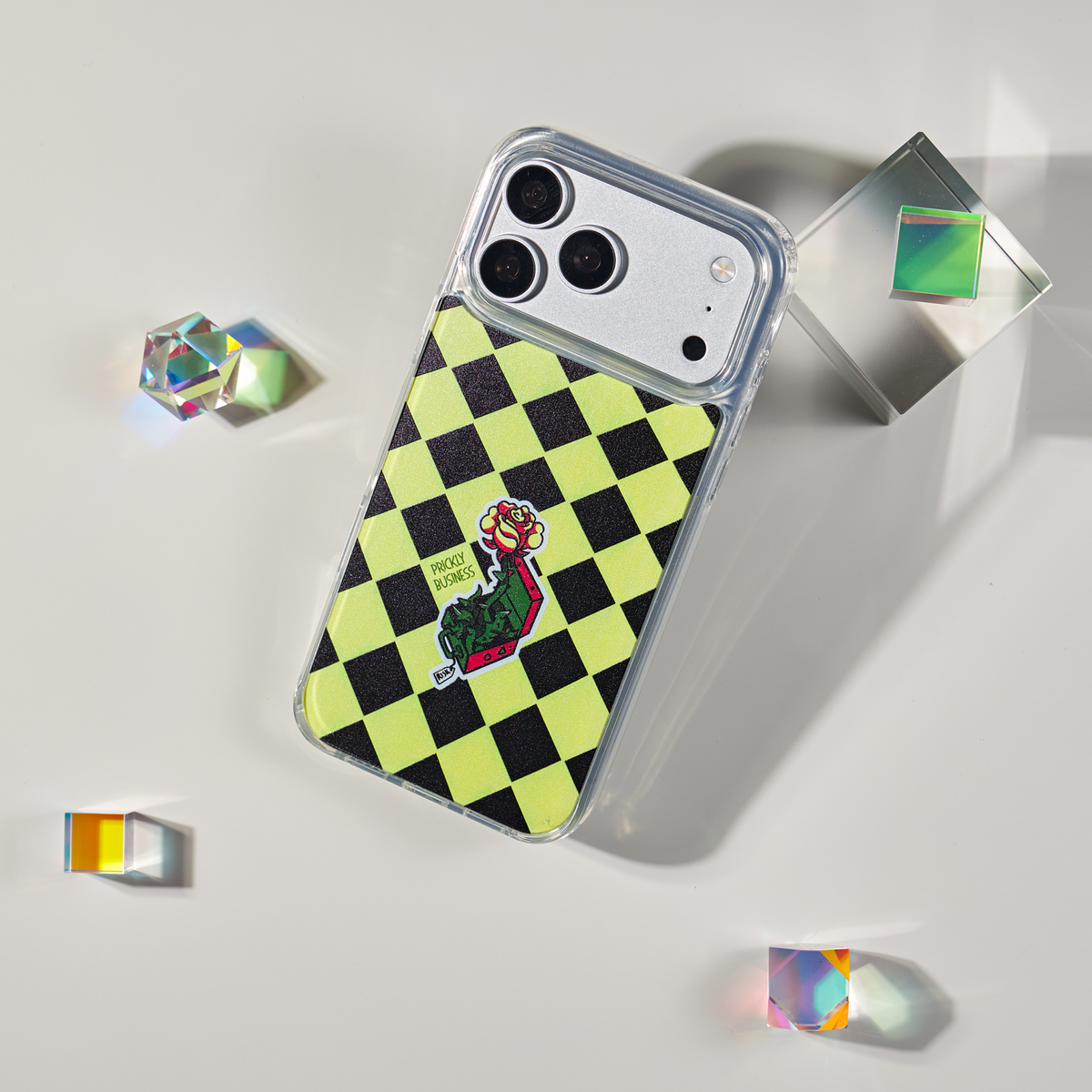 Freehand Case in Prickly Business for iPhone 18 Pro Max, chartreuse and black checkerboard design, shown at an angle with crystal props.
