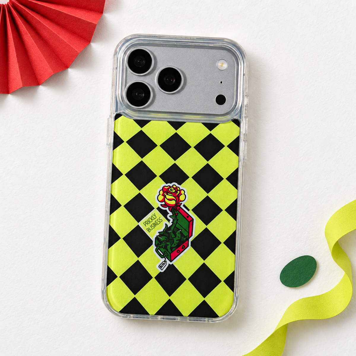 Freehand Case in Prickly Business for iPhone 18 Pro Max, chartreuse and black checkerboard design, in a playful colored-paper scene.