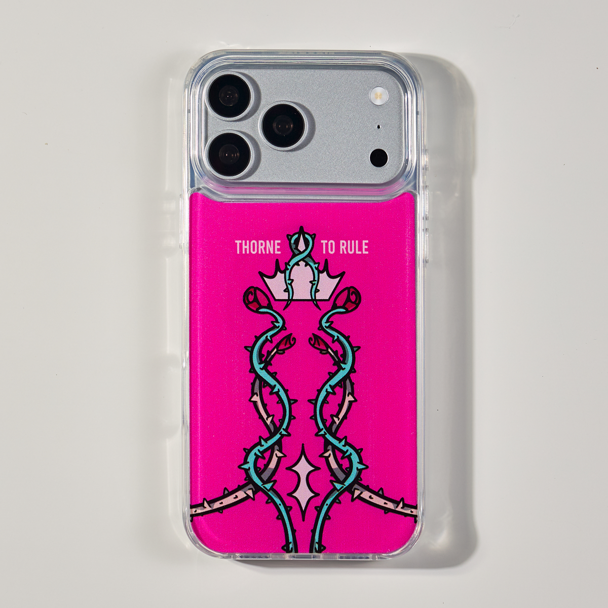 Freehand Case in Thorn Royalty for iPhone 18 Pro Max, pink design with twisting thorn vines and a crown, shown from the back on a neutral studio background.
