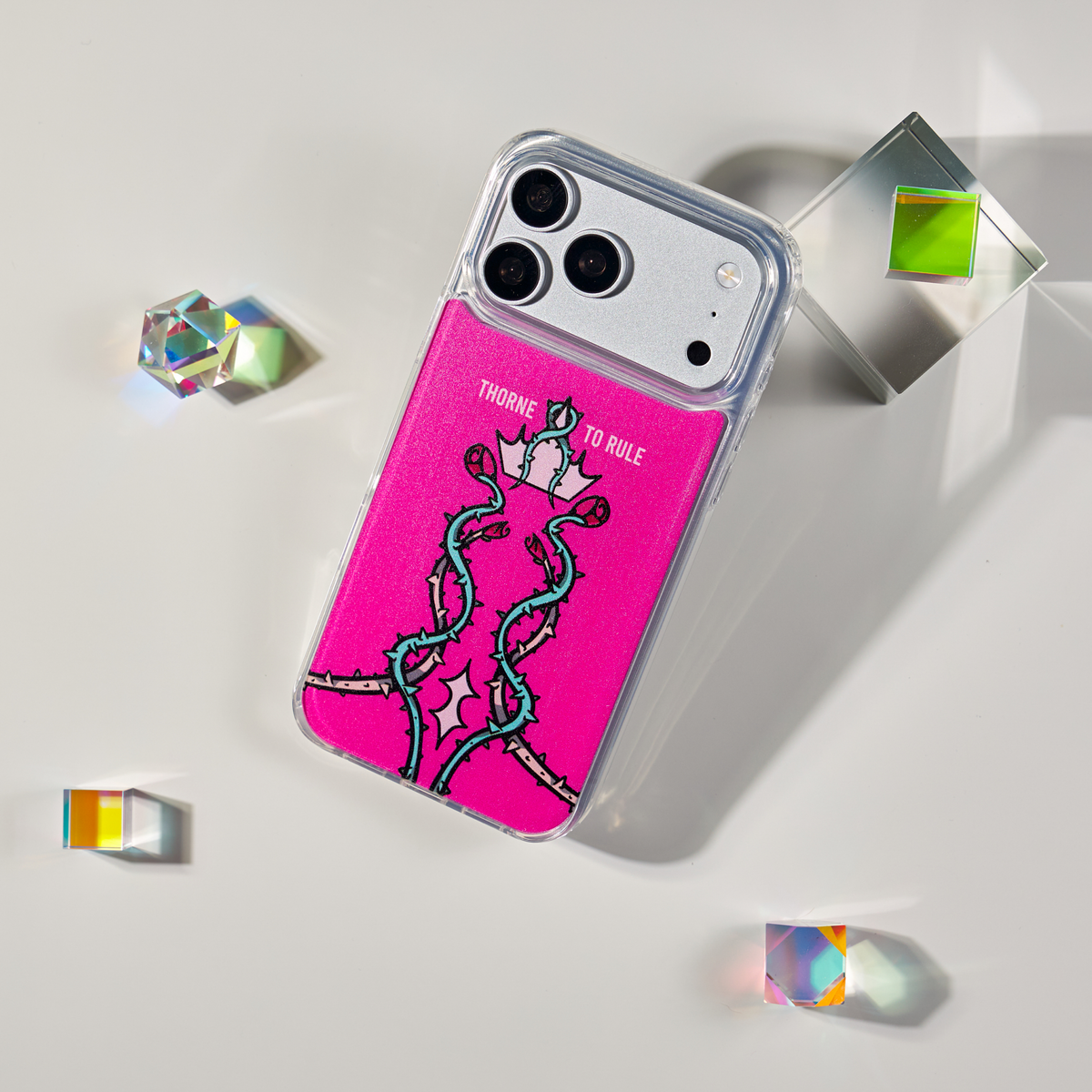 Freehand Case in Thorn Royalty for iPhone 18 Pro Max, pink design with twisting thorn vines and a crown, shown at an angle with crystal props.