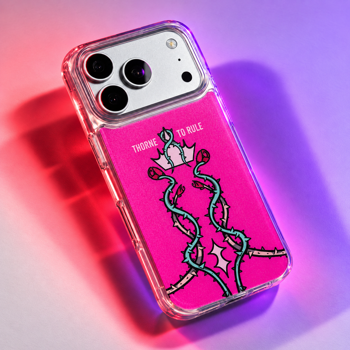Freehand Case in Thorn Royalty for iPhone 18 Pro Max, pink design with twisting thorn vines and a crown, under colored gel studio lighting.