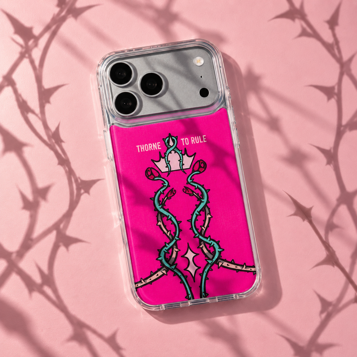 Freehand Case in Thorn Royalty for iPhone 18 Pro Max, pink design with twisting thorn vines and a crown, with patterned studio light and shadows.