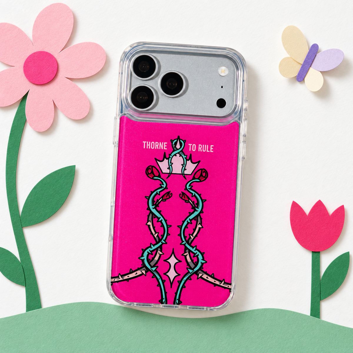 Freehand Case in Thorn Royalty for iPhone 18 Pro Max, pink design with twisting thorn vines and a crown, in a playful colored-paper scene.