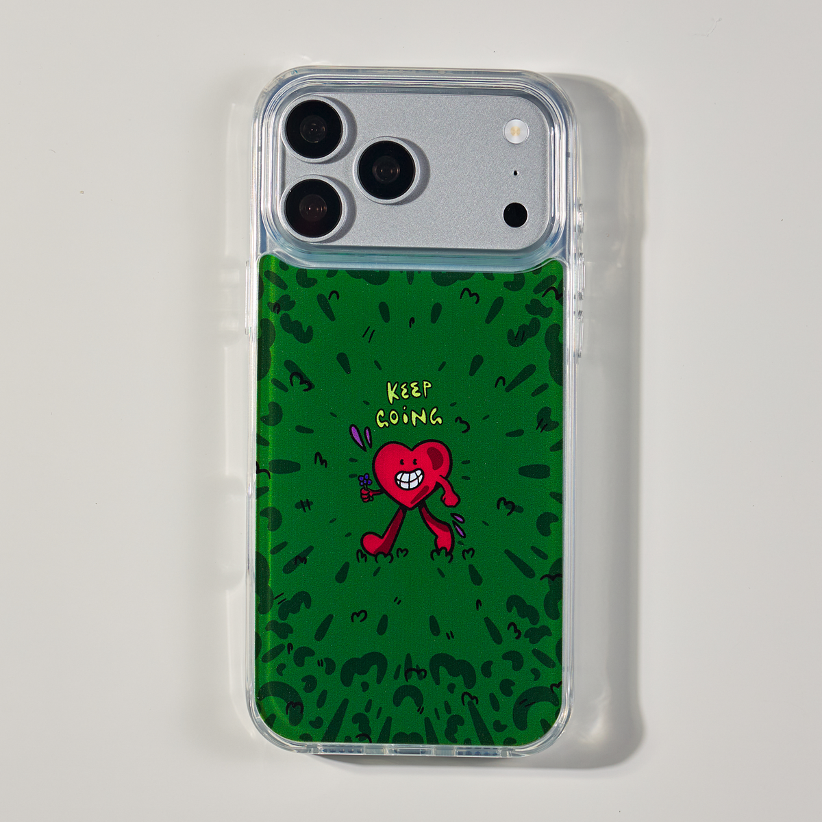 Freehand Case in Wild Heart for iPhone 18 Pro Max, green doodle design with a red walking heart, shown from the back on a neutral studio background.