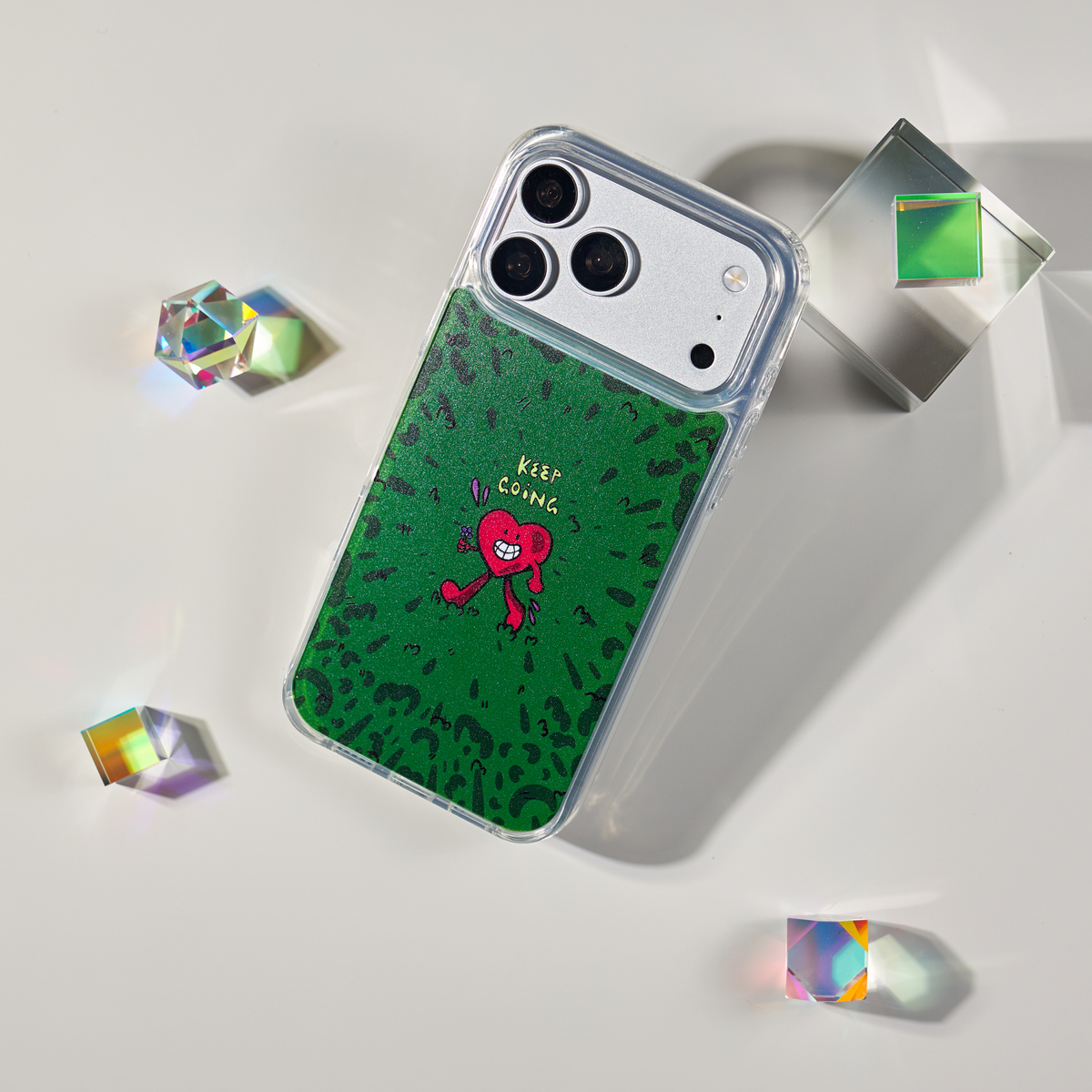 Freehand Case in Wild Heart for iPhone 18 Pro Max, green doodle design with a red walking heart, shown at an angle with crystal props.